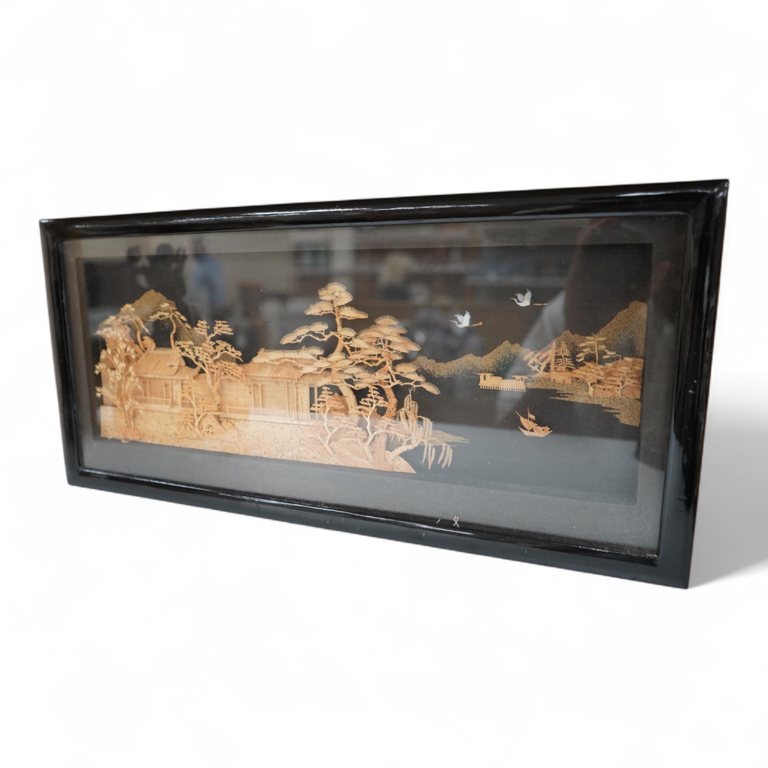A Chinese framed, intricate relief cork landscape carving, of a Pagoda amongst trees by a river with junks and birds above., 41cm x 15cm